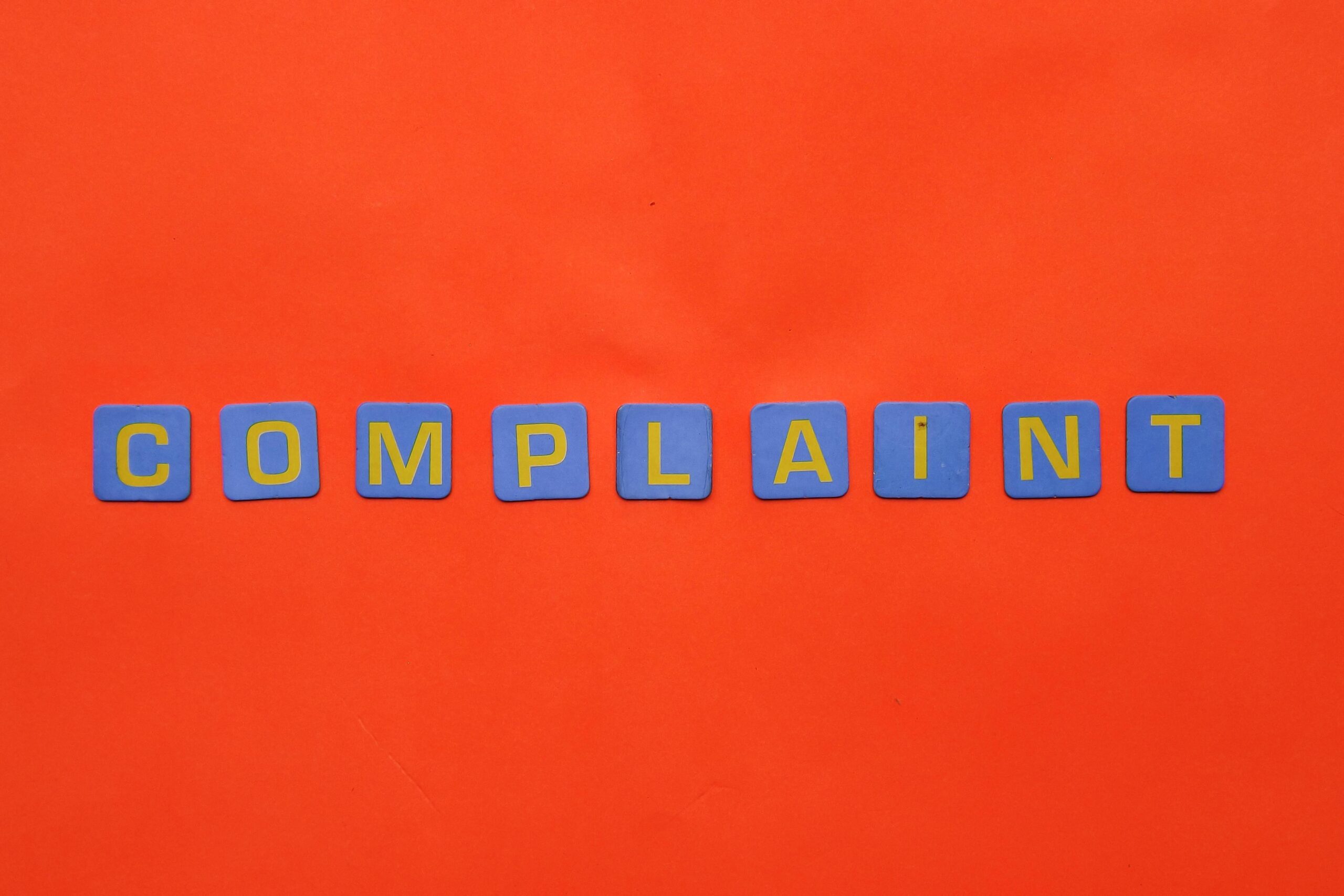 Blue letter tiles spelling 'COMPLAINT' on a vibrant red surface.